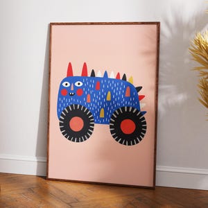 以下が含まれることがあります： フレームに入ったアートプリント。空想的なモンスターカーのイラストが描かれています。トラックは青色で、カラフルなアクセント、赤い中心部を持つ大きな黒い車輪、遊び心のあるデザインです。背景はソフトピンクです。