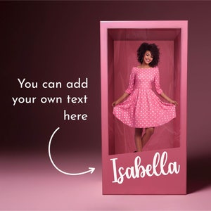 May include: A pink dollhouse with a woman in a pink polka dot dress standing inside. The dollhouse has a white inscription that says "Isabella".