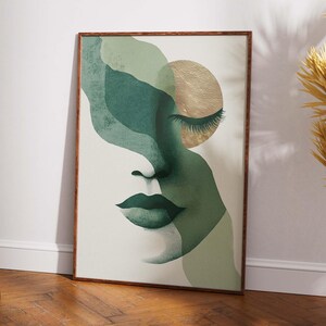 May include: Abstract art print featuring a woman's face in shades of green and gold. The artwork has a minimalist style with a closed eye, full lips, and a gold circle. The print is framed in a brown wooden frame.