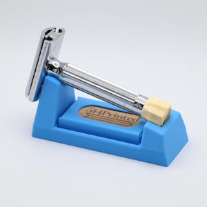 May include: A chrome safety razor with a white plastic handle is resting on a blue plastic stand. The stand has a brown label with the text "514Printed" on it.