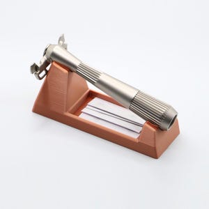 May include: A silver safety razor with a textured handle sits on a brown plastic stand. The stand has a slot for razor blades.