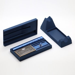K&ouml;nnte beinhalten: Ein mattes marineblaues Rasierhobel-Set bestehend aus einem zerlegten Griff, einem Rasierkopf mit Gewindestift, einem rechteckigen Aufbewahrungsetui mit Deckel und einem St&auml;nder. Eine kleine Metallklingenpackung mit der Aufschrift RK liegt im Etui.