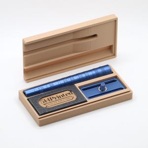 K&ouml;nnte beinhalten: Ein blauer Sicherheitsrasierer-Griff und Kopfkomponenten in einem beigen Kunststoffetui. Das Etui enth&auml;lt einen schwarzen Einsatz mit dem Text 514Printed und Push and Slide to Open. Der Rasiergriff weist ein strukturiertes Griffmuster auf.