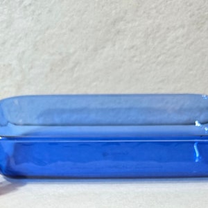 May include: A blue glass baking dish with a rectangular shape and two handles on the sides. The dish is empty and appears to be made of tempered glass.