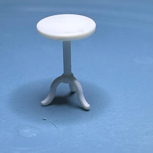 May include: A white plastic table with a round top and three legs. The table is about 10 inches tall.