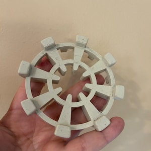 May include: A white plastic drain cover with a circular design and multiple openings. The cover has a textured surface.