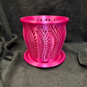 May include: A pink plastic planter with a decorative leaf pattern. The planter has a matching saucer.