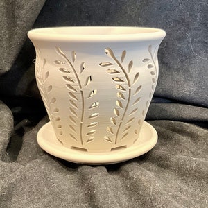 May include: White ceramic planter with a leafy design. The planter has drainage holes and a matching saucer.