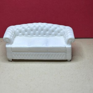 May include: A miniature white sofa featuring a tufted backrest and rolled arms. The piece has a detailed button-tufted design on the back and front base, with a smooth seat cushion surface. This small furniture item is rendered in a solid white color.