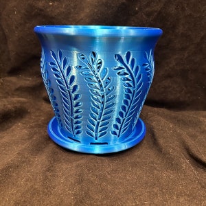May include: A blue plastic planter with a decorative leaf pattern. The planter has a drainage tray.