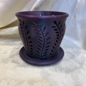 May include: A purple ceramic planter with a decorative leaf pattern. The planter has a matching saucer.
