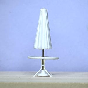 May include: A miniature white patio table with a matching umbrella. The umbrella is closed and has a ridged design. The table has a round top and a pedestal base. The table and umbrella are made of plastic.