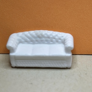 May include: A miniature white sofa featuring a tufted backrest, rolled arms, and a smooth seat cushion. The piece is rendered in a solid white material with a detailed texture on the back and base, showcasing a classic three-seat design.