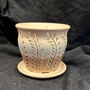 May include: A white ceramic planter with a leaf design. The planter has a saucer and is made of a light-colored ceramic.