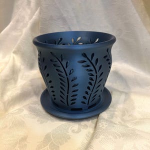 May include: A navy blue ceramic planter with a matching saucer. The planter features a cut-out leaf design around the sides. The planter is designed for indoor or outdoor use.