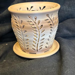 May include: A ceramic planter with a decorative leaf design. The planter has a light brown glaze and a matching saucer.