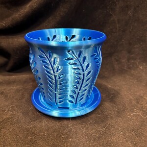 May include: A blue plastic planter with a decorative leaf pattern. The planter has a removable base.