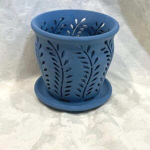 May include: A blue ceramic planter with a matching saucer. The planter features a cut-out leaf design around the sides. The planter is approximately 5 inches in diameter and 4 inches tall.