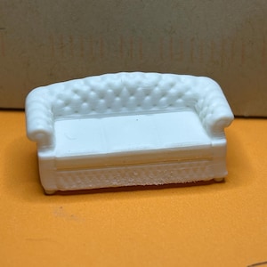 May include: A miniature white sofa featuring a tufted backrest, rolled arms, and a smooth seat cushion. The piece has a detailed quilted texture on the front base and back, designed as a small-scale model for display or hobbyist projects.