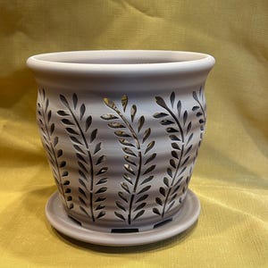 May include: A light gray ceramic planter with a leaf design. The planter has drainage holes and comes with a matching saucer.
