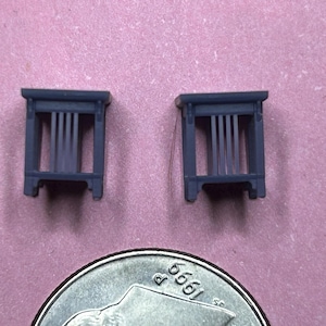 May include: Two small, dark gray, wooden, decorative, miniature, open-top, rectangular, framed structures with vertical slats. The structures are approximately the size of a US quarter.