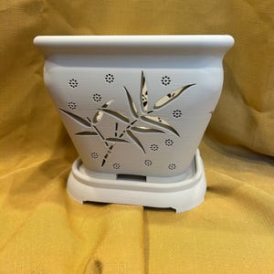 May include: White ceramic planter with a bamboo design and drainage holes. The planter has a matching saucer.