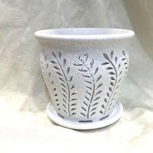 May include: A speckled, light gray ceramic planter with a matching saucer. The planter features a cut-out leaf design around the sides. The pot has a wide opening and is suitable for indoor or outdoor use. The planter is approximately 6 inches tall.