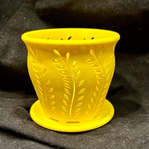 May include: A bright yellow plastic planter with a decorative leaf design. The planter has a matching saucer.