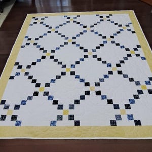 May include: A rectangular quilt featuring a white background with a lattice pattern of small dark blue and black squares. The intersections of the lattice are marked by small yellow squares. The quilt is finished with a wide yellow border.