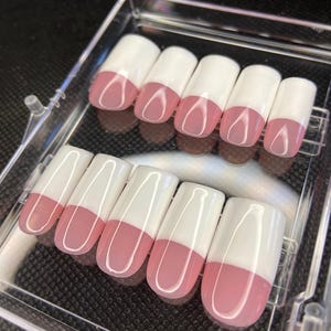 May include: A set of ten false nails with a white tip and a pink base. The nails are arranged in two rows in a clear plastic case.