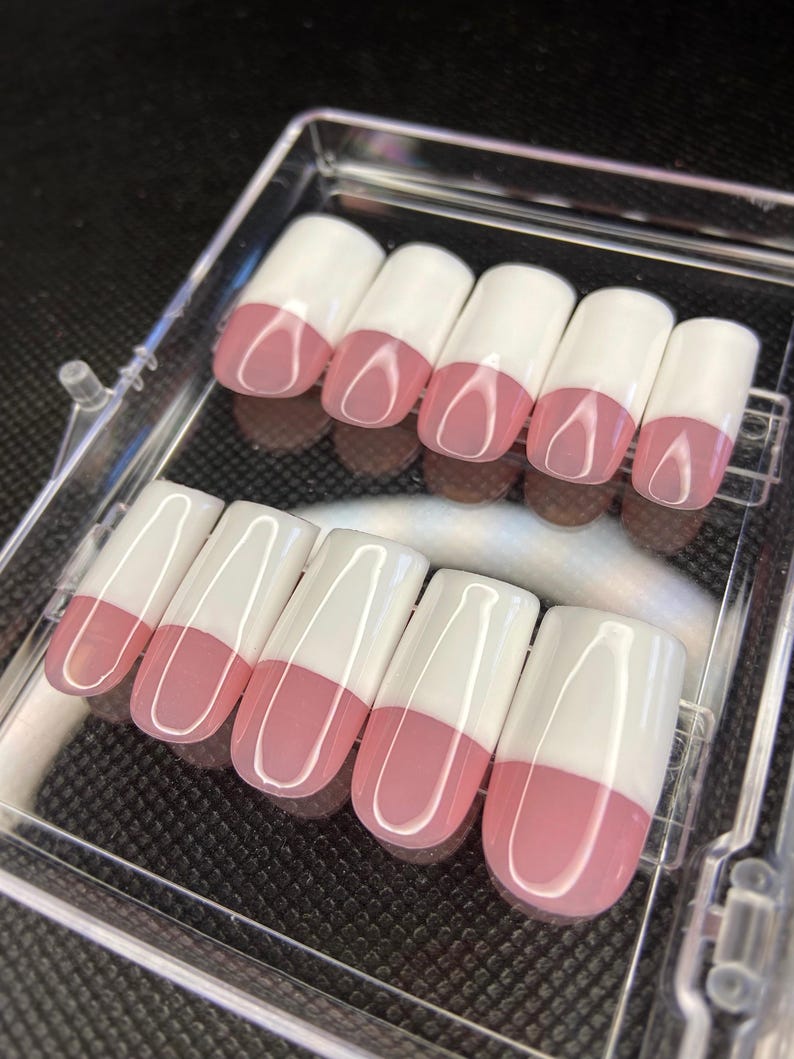 May include: A set of ten false nails with a white tip and a pink base. The nails are arranged in two rows in a clear plastic case.