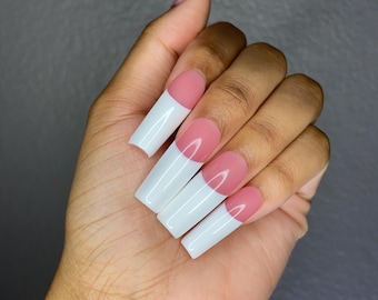 May include: A set of long, white and pink acrylic nails with a half-moon design. The nails are long and pointed, with a white tip and a pink base.