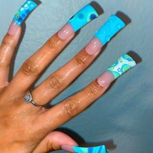 May include: Long, blue and white painted nails with a variety of designs, including swirls, stars, and circles.