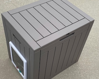 May include: A gray, rectangular pet house with a slatted top and vertical side panels. It features a small pet door with a white frame and a clear flap. The house has a handle on top.