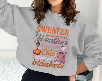 Może przedstawiać: Jasnoszara bluza z nadrukiem w jesiennym klimacie. Grafika zawiera słowa "SWEATER Weather" oraz inne słowa związane z jesienią, takie jak "pumpkin spice", "bonfires", "apple pie" i "blankets". Grafika zawiera również ilustracje dyni, żołędzia, kubka kawy i swetra.