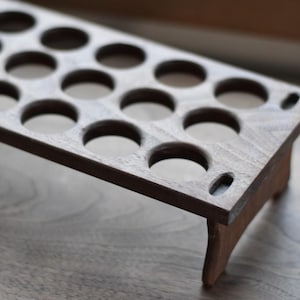 Pode incluir: Um suporte de exibi&ccedil;&atilde;o de madeira com v&aacute;rios orif&iacute;cios circulares. O suporte &eacute; feito de madeira marrom escura e tem uma forma retangular com pequenas pernas. Os orif&iacute;cios s&atilde;o espa&ccedil;ados uniformemente.
