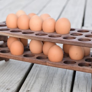 Pode incluir: Um suporte de madeira para ovos de dois n&iacute;veis cheio de ovos castanhos. O suporte castanho escuro tem recortes circulares para segurar os ovos. Os ovos s&atilde;o de cor castanha clara e est&atilde;o uniformemente espa&ccedil;ados no suporte.