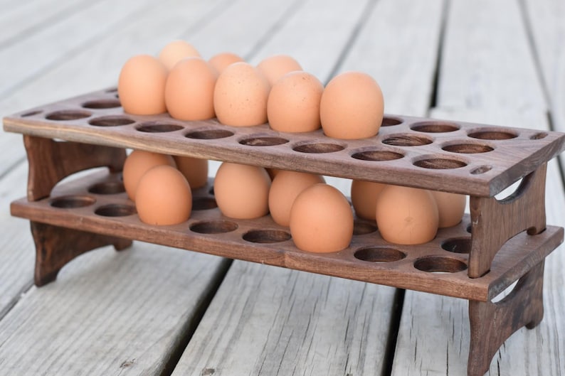 Pode incluir: Um suporte de madeira para ovos de dois n&iacute;veis cheio de ovos castanhos. O suporte castanho escuro tem recortes circulares para segurar os ovos. Os ovos s&atilde;o de cor castanha clara e est&atilde;o uniformemente espa&ccedil;ados no suporte.