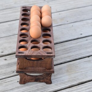 Pode incluir: Um suporte de madeira para ovos de dois n&iacute;veis, feito de madeira castanha escura. O suporte foi projetado para acomodar ovos, com v&aacute;rios ovos castanhos vis&iacute;veis no n&iacute;vel superior. Uma solu&ccedil;&atilde;o de armazenamento de cozinha pr&aacute;tica e elegante.
