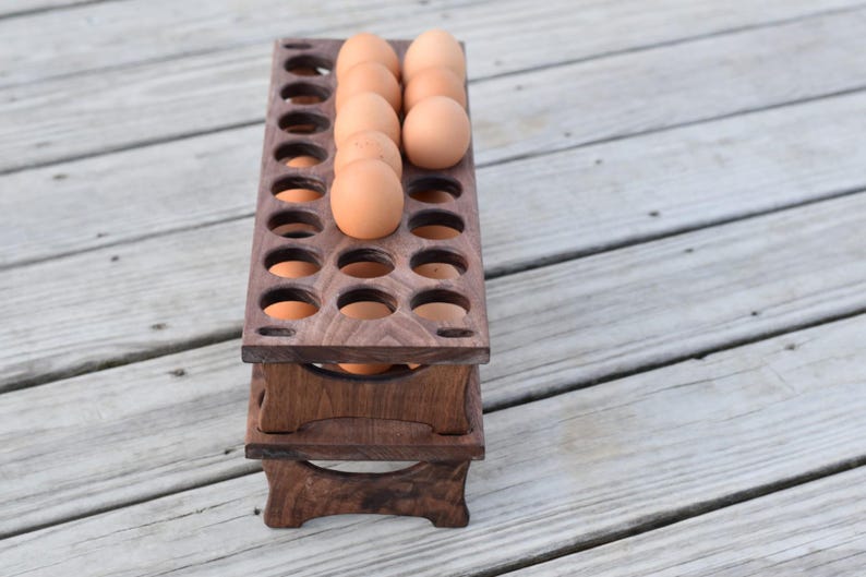 Pode incluir: Um suporte de madeira para ovos de dois n&iacute;veis, feito de madeira castanha escura. O suporte foi projetado para acomodar ovos, com v&aacute;rios ovos castanhos vis&iacute;veis no n&iacute;vel superior. Uma solu&ccedil;&atilde;o de armazenamento de cozinha pr&aacute;tica e elegante.