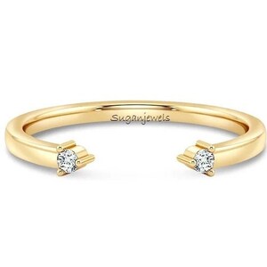 Op de afbeelding: Een gouden ring met twee kleine diamanten aan de uiteinden. De ring is aan één kant open, waardoor hij verstelbaar is.