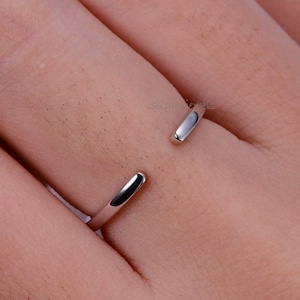 Puede incluir: Un anillo de plata simple con un diseño minimalista. El anillo está abierto por un lado y tiene un acabado liso y pulido.