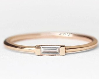 May include: A delicate rose gold band ring with a single, small, rectangular-shaped diamond set in the center.