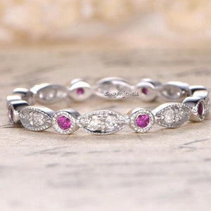 May include: A delicate eternity band featuring a row of alternating round pink sapphires and oval-shaped diamonds set in a white gold band.
