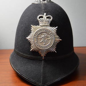 May include: A black police helmet with a silver badge that reads "Somerset and Bath Constabulary" and a silver crown on top.