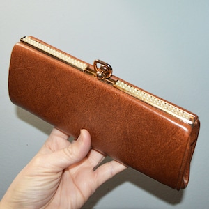 May include: A brown leather clutch purse with a gold clasp and a row of white pearls along the edge.