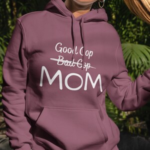 Puede incluir: Una sudadera con capucha color granate con un gráfico blanco que dice "Good Cop - Bad Cop MOM".
