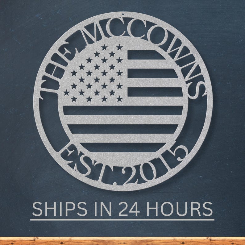 May include: A silver metal wall art piece featuring a circular design with the American flag in the center. The text "THE MCCOWNS EST. 2015" is cut out around the flag. The piece is displayed against a dark blue background.