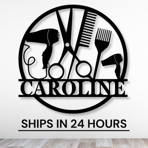 May include: Black metal circle sign with a hair dryer, scissors, comb, and hair pick. The sign says "CAROLINE" in a decorative font.