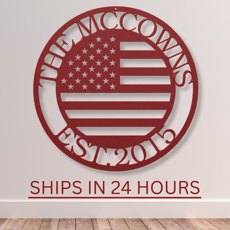 May include: A red metal wall art piece featuring the American flag design within a circular frame. The text "THE MCCOWNS EST. 2015" is inscribed around the flag. The piece is mounted on a white wall.